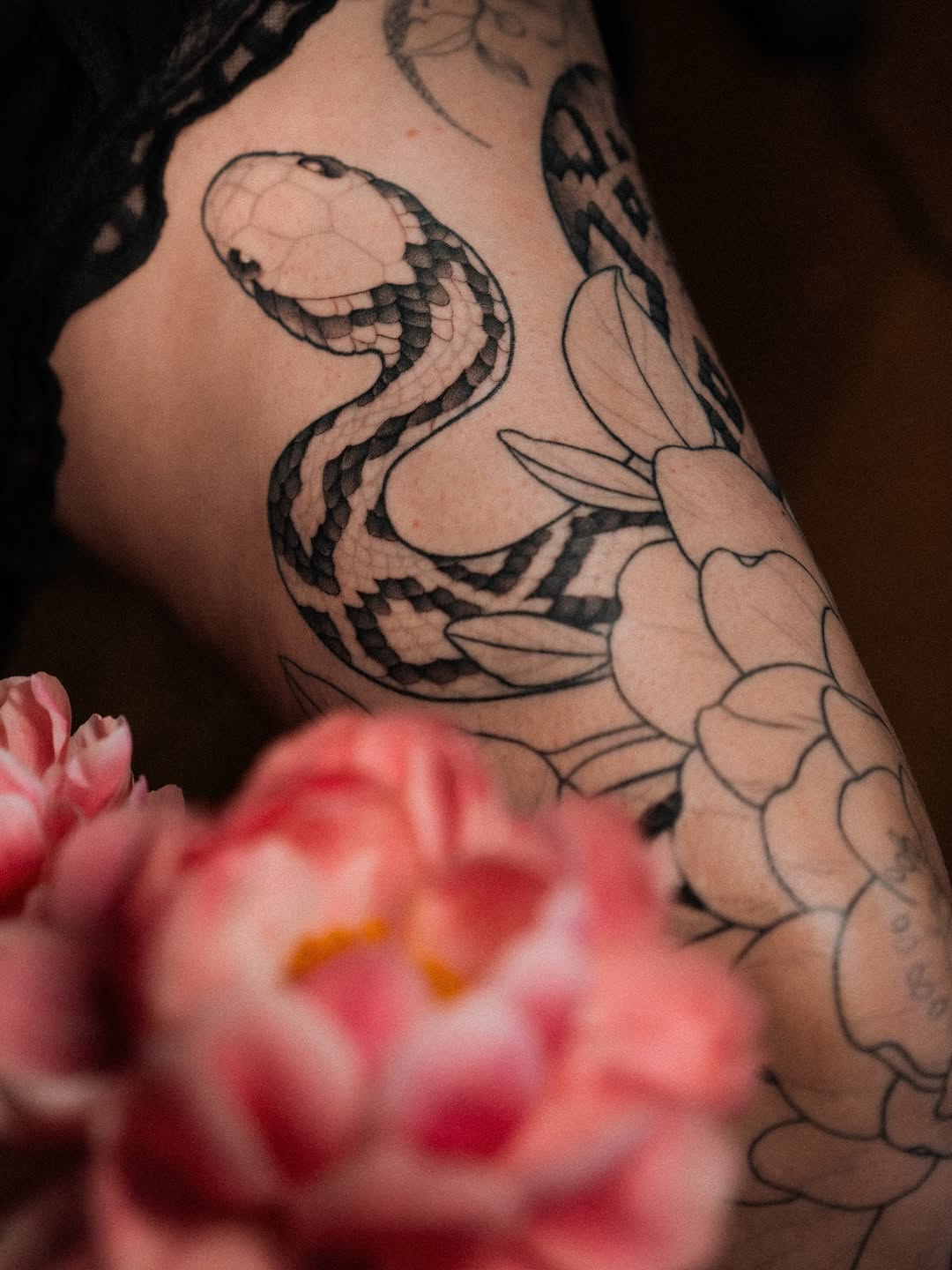 Snake coiled around flowering lotus on upper arm with soft black and grey shading, pink flower in foreground.