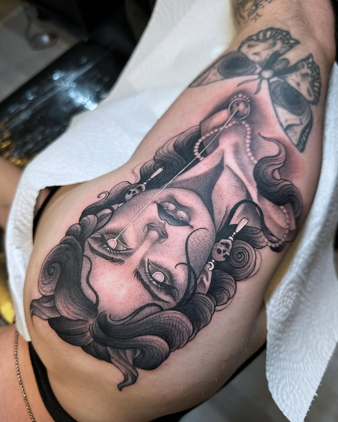Two-faced female portrait with flowing dark hair and ornate jewelry on upper arm, rendered in black and grey with soft shading.