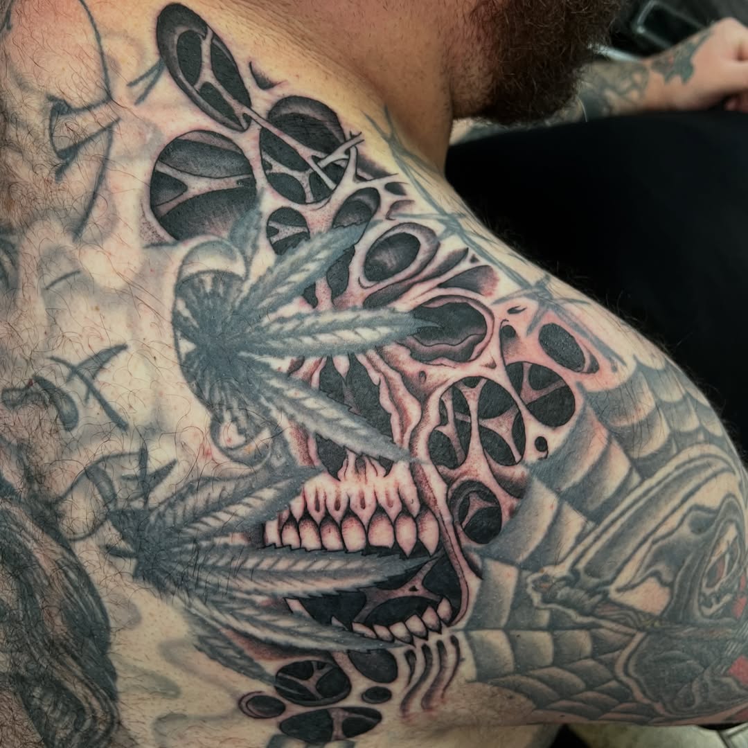 Ornate skull with feathered wings and geometric eye sockets in black and grey shading on chest.