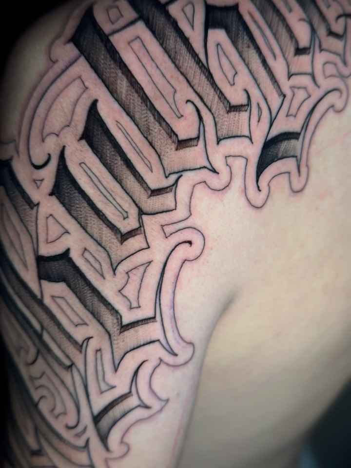 Black and grey abstract geometric tattoo with curved layered shapes and cross-hatching on upper arm, featuring dimensional shading.