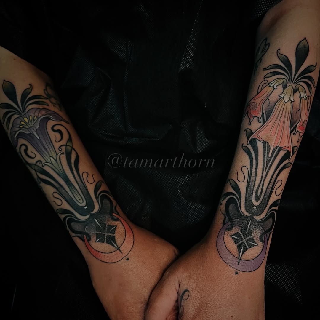Matching forearm tattoos featuring ornate floral designs with feminine figures in flowing robes and decorative elements in black and grey shading.