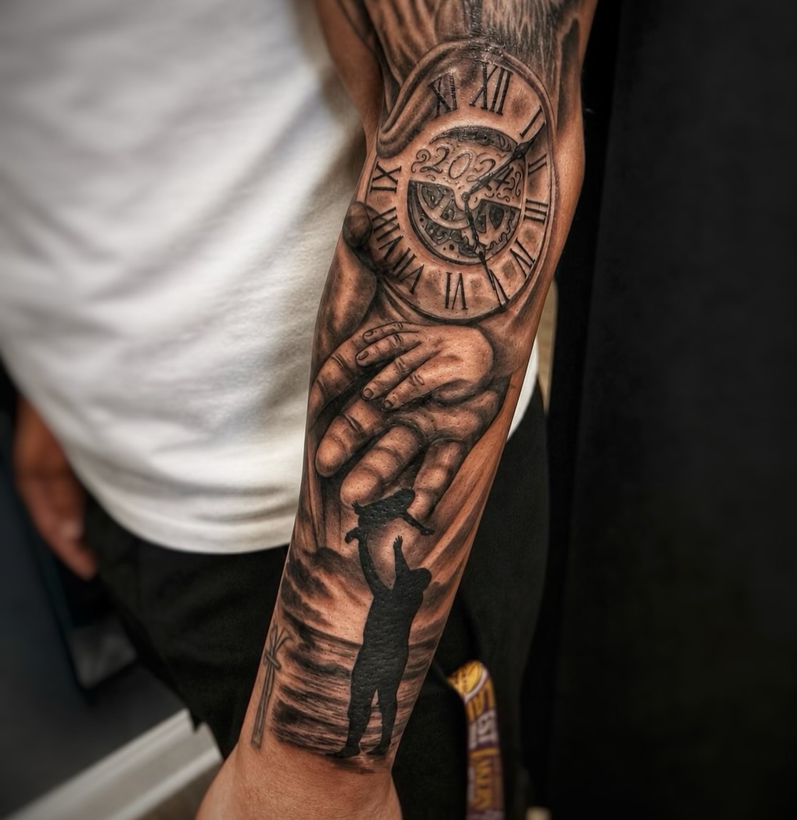 Full forearm sleeve tattoo featuring a detailed clock with Roman numerals showing 2024, a reaching hand, and a silhouetted figure below in black and grey shading.