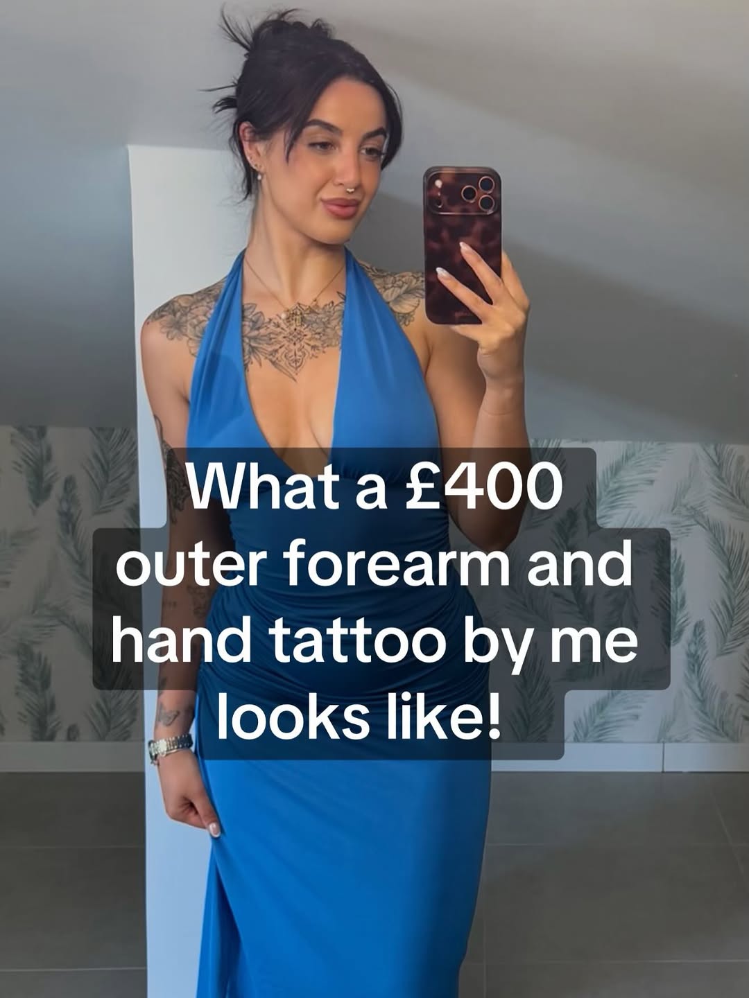 Ornate black and grey chest and outer forearm tattoo with intricate geometric and floral patterns on a woman in blue halter dress.