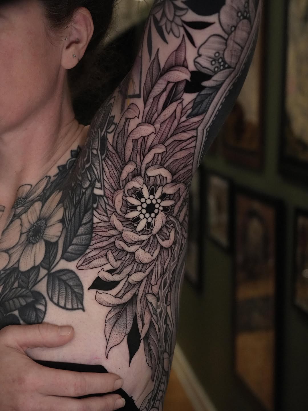 Black and grey floral sleeve tattoo featuring detailed flowers with layered petals and leaves on upper arm.