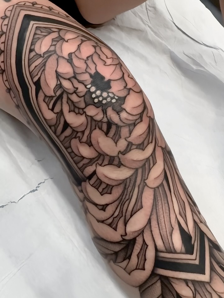 Large black and grey wing tattoo with detailed feather work and ornamental borders on upper arm.