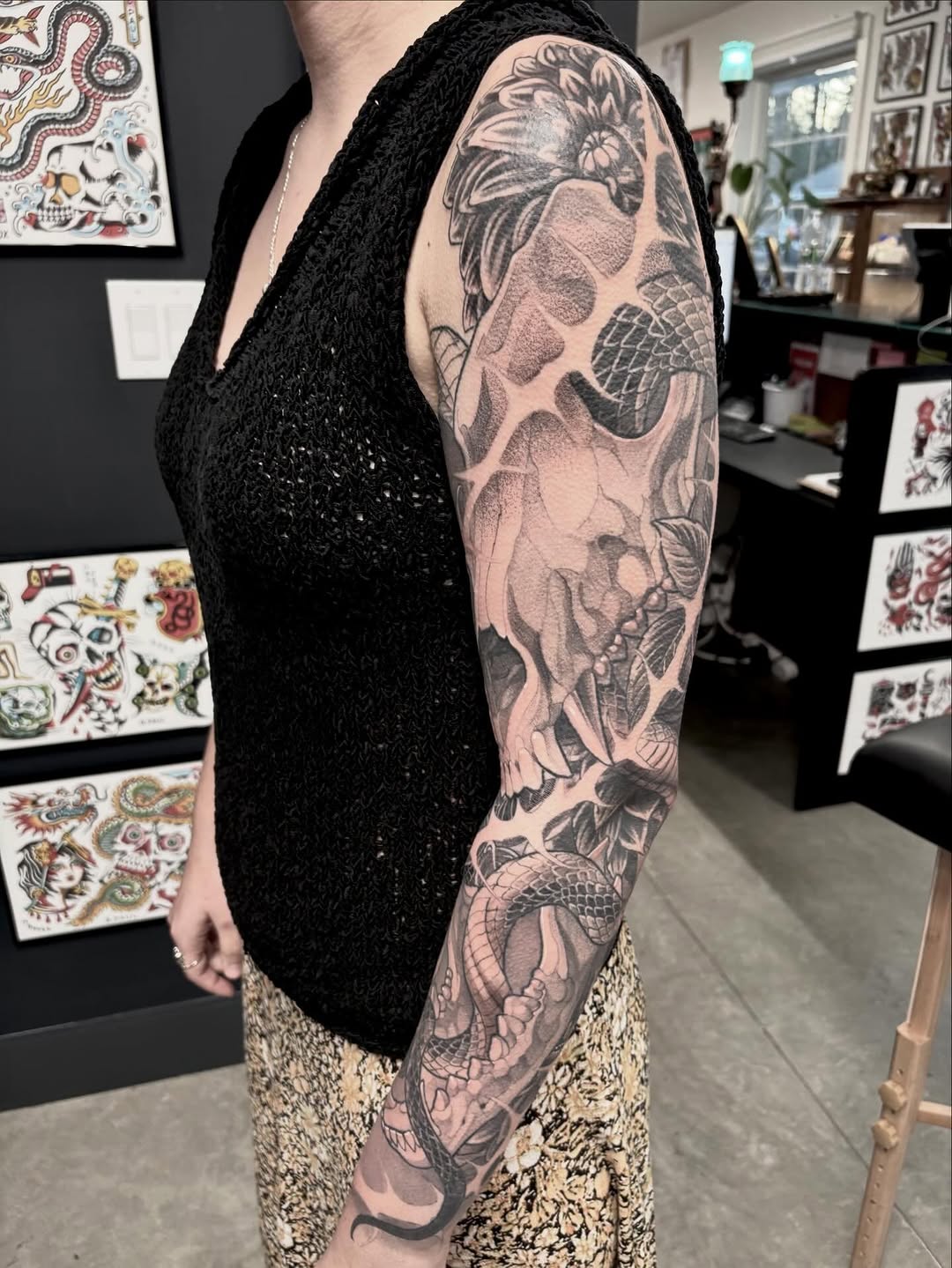 Black and grey full sleeve tattoo featuring a koi fish, skull, and floral elements with detailed shading on the arm.