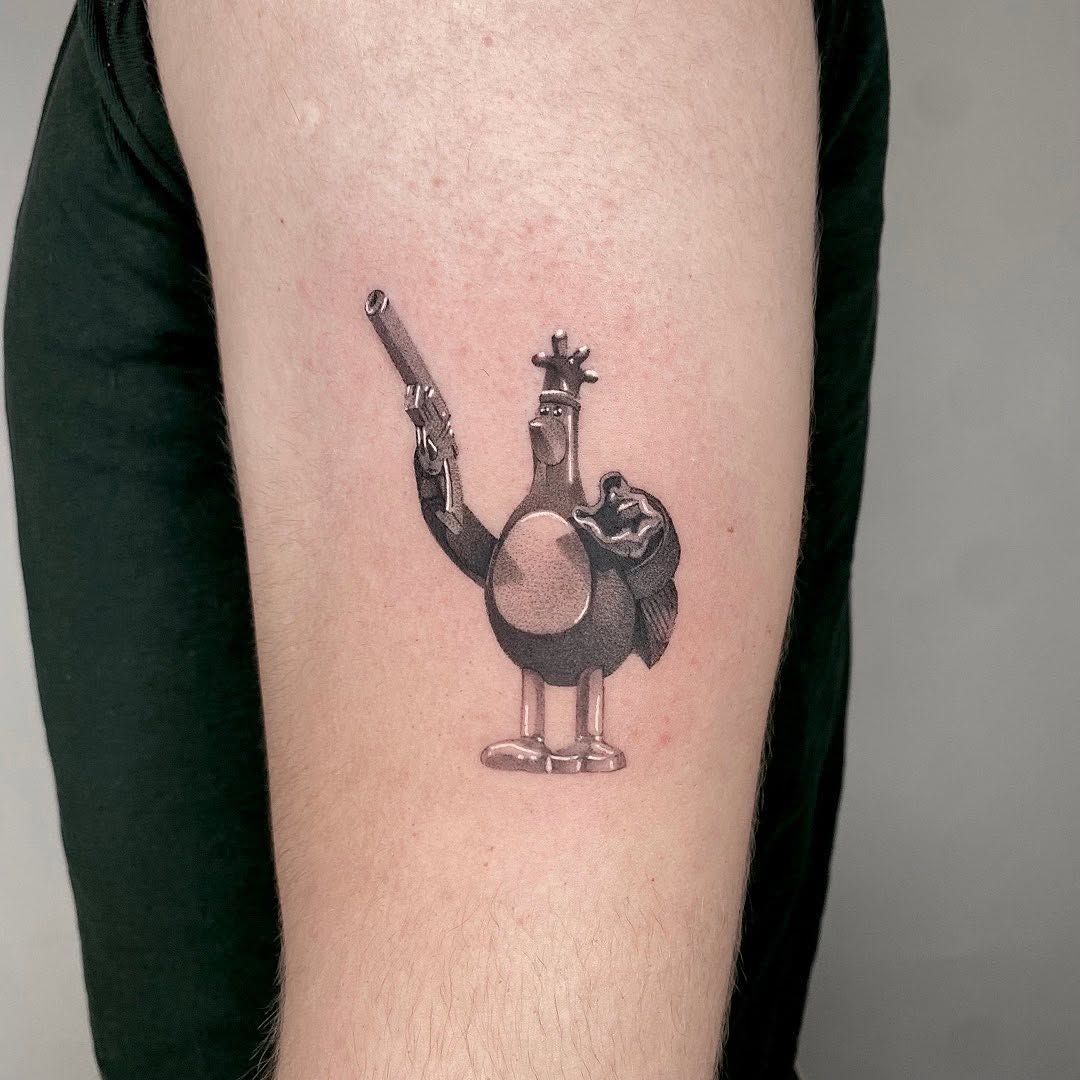 A whimsical character with a large round body holding a revolver and star, rendered in black and grey shading on an upper arm.